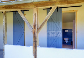 Outdoor bathroom area with blue sliding barn doors and a visible toilet by the glamping tent at Domaine La Barbe.
