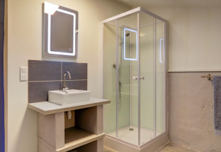 Bathroom in a glamping tent at Domaine La Barbe, France, featuring a shower, sink, and illuminated mirror.