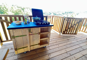 Cuisine extérieure sur terrasse en bois avec réchaud et ustensiles dans une tente glamping à Domaine La Barbe, France.