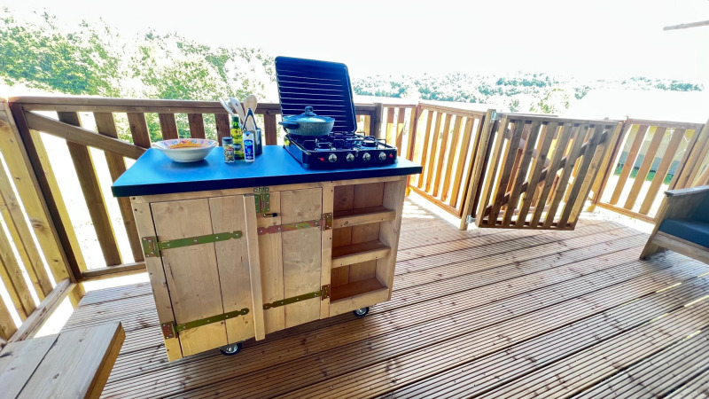 Buitenkeuken op houten terras met fornuis en keukengerei bij een glampingtent op Domaine La Barbe, Frankrijk.