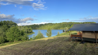 Glamping tent bij Domaine La Barbe in Frankrijk met uitzicht op een meer en groene bosrijke omgeving.