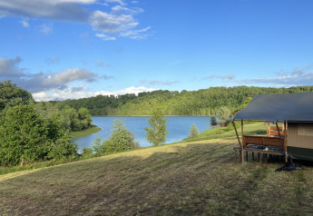 Udsigt over glamping telt ved Domaine La Barbe i Frankrig med sø og grønne træer i baggrunden.
