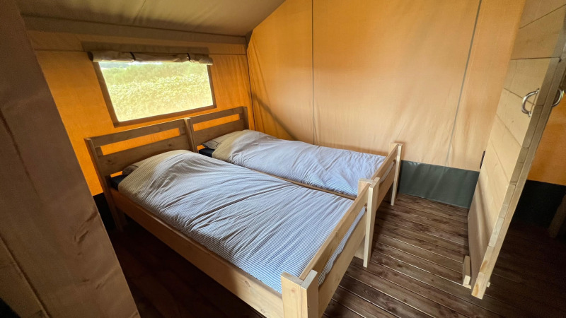 Interior de una tienda glamping tipo safari en Domaine La Barbe, Francia, con dos camas individuales de madera.