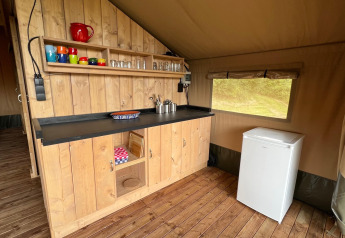 Angolo cucina in una tenda safari glamping presso Domaine La Barbe, Francia, con mobile in legno e frigorifero.