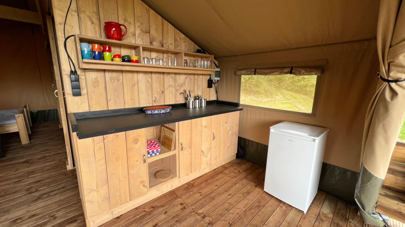 Angolo cucina in una tenda safari glamping presso Domaine La Barbe, Francia, con mobile in legno e frigorifero.