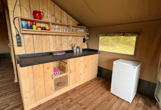 Kitchen area in a glamping safari tent at Domaine La Barbe in France, featuring wood cabinet and minifridge.