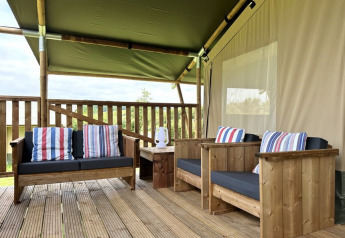 Holzterrasse mit Safari-Zelt, bequemen Sesseln, bunten Kissen und Tisch im Domaine La Barbe, Frankreich.
