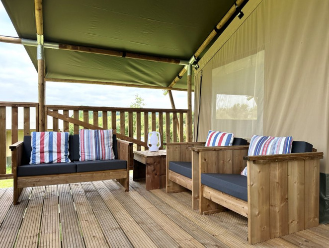 Udendørs terrasse med træsofaer, farverige puder og et bord under en safari glamping-telt i Domaine La Barbe.