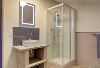 Baño moderno en tienda glamping en Domaine La Barbe, Francia, con cabina de ducha y lavabo.