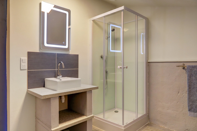 Salle de bain moderne sous tente glamping au Domaine La Barbe, France, avec cabine de douche et lavabo.