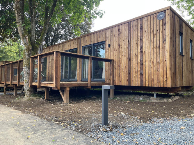 Ecolodge XXL TERRAS im Hameau de l'Ourthe, Belgien – moderne Holzlodge mit Terrasse, umgeben von Bäumen.