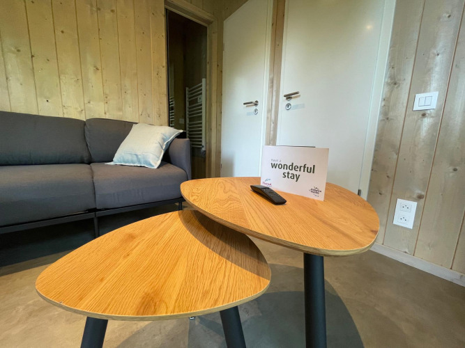 Sala moderna con paredes de madera, sofá, mesas bajas y tarjeta de bienvenida en Ecolodge XXL TERRAS, Bélgica.
