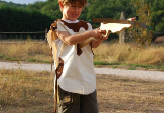Jongen speelt buiten met houten kruisboog op Flower Camping La Sagne, vakantiepark in Nouvelle-Aquitaine, Frankrijk.