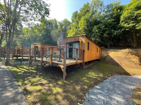 Eco Lodge ved Hameau de l'Ourthe i Belgien, en hyggelig træhytte med terrasse omgivet af grøn natur.