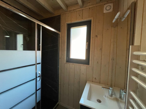 Moderne badeværelse med træpaneler, brusekabine, vindue og håndvask på Eco Lodge i Hameau de l'Ourthe, Belgien.