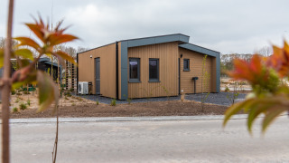 Photo of Cube Split Hottub lodge featuring modern wood paneling, gray trim, and newly planted shrubs.