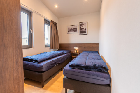 Due letti singoli con copriletto blu scuro in una stanza luminosa al Cube Split Hottub, EuroParcs Enkhuizer Strand.