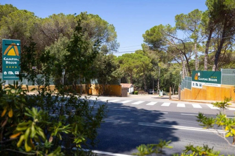 Entrance to Camping Begur holiday park in Catalonia, Spain, with signs, road, and trees in the background.