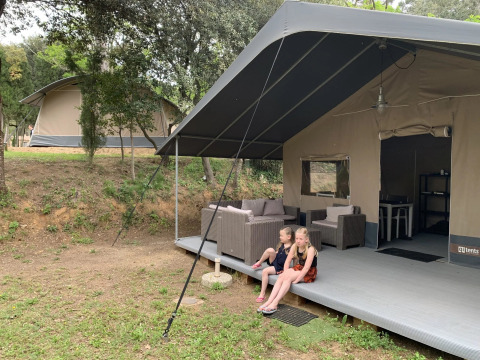 Due bambini seduti davanti a una tenda al Camping Begur in Catalogna, Spagna, tra gli alberi.