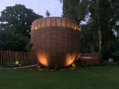 Træbeklædt tiny house ved navn The Nutshell med spabad og sauna i en grøn park i Holland, aftenstemning.