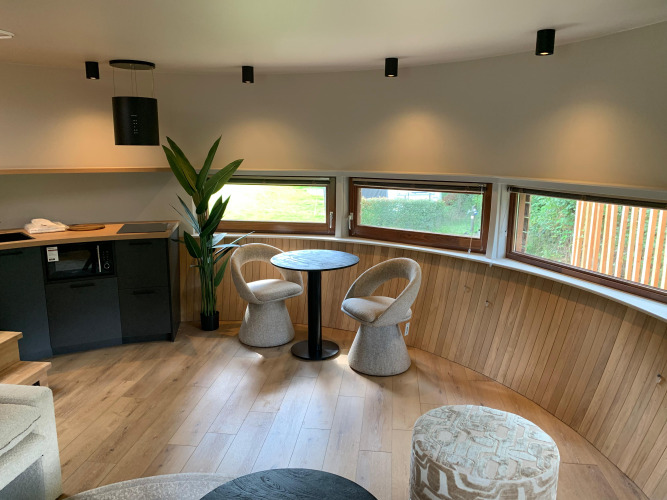 Interior de The Nutshell tiny house con mesa redonda, sillas y ventanas en Recreation Park Den Blanken.