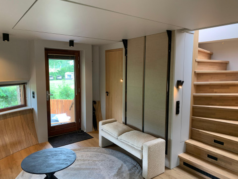 Moderne tiny house-stue med trapper, sofa, rundt tæppe og udsigt til grønt område hos Den Blanken.