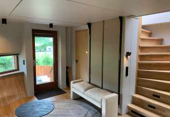 Sala de tiny house moderna con escaleras, sofá, alfombra redonda y vista verde en Den Blanken, Países Bajos.