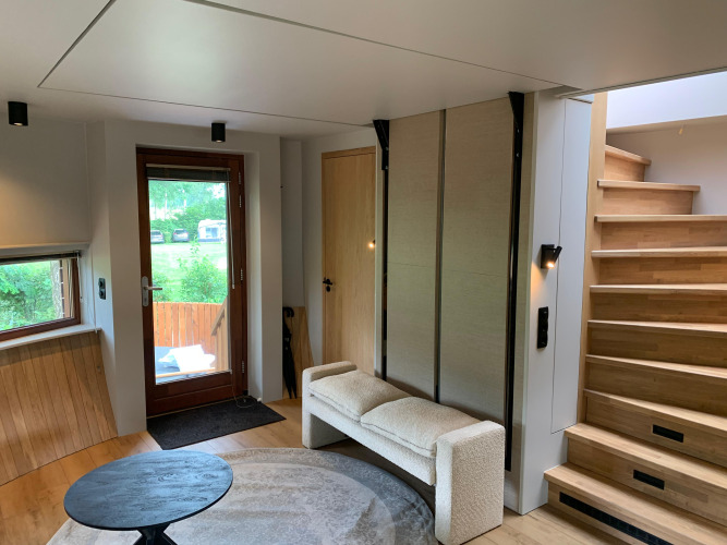 Sala de tiny house moderna con escaleras, sofá, alfombra redonda y vista verde en Den Blanken, Países Bajos.