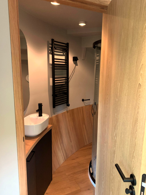 Tiny house bathroom at The Nutshell with wood accents, vessel sink, black towel rail, and glass shower.