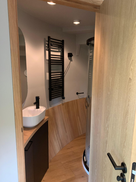 Kleine badkamer in The Nutshell met moderne wasbak, zwarte handdoekdroger en houten afwerking.