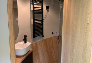 Lille badeværelse i The Nutshell med moderne inventar, håndvask, sort håndklædetørrer og bruser.