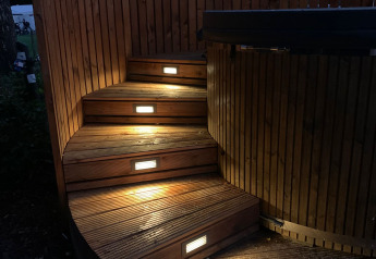 Beleuchtete Holztreppe und Whirlpool im Freien bei The Nutshell im Recreation Park Den Blanken, Niederlande.