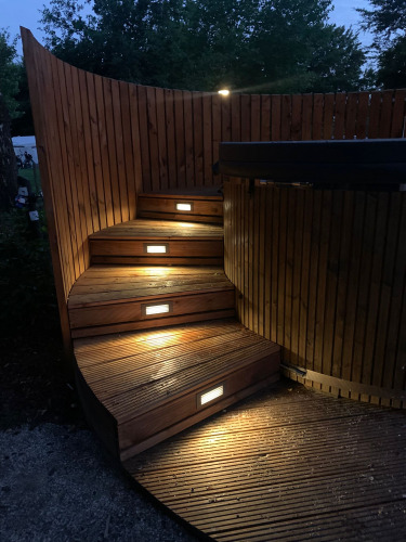 Escaleras curvas de madera iluminadas junto a un jacuzzi en The Nutshell en Den Blanken, Países Bajos.
