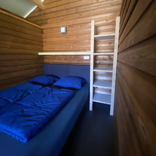 Intérieur d'une tente safarilodge deluxe avec murs en bois, lit double et échelle au parc Krieghuusbelten, Pays-Bas.