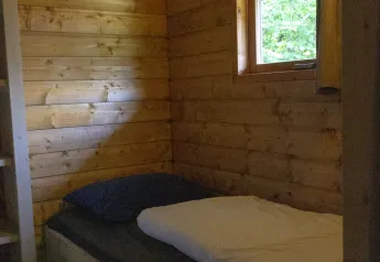 Stanza in legno con letto singolo, cuscino e finestra in una safarilodge deluxe nei Paesi Bassi.