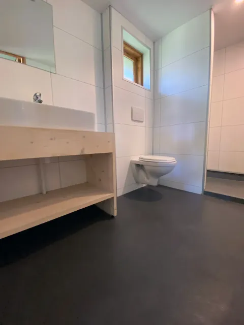 Modern bathroom with wall-mounted toilet, wooden sink stand and small window at Safarilodge deluxe.