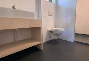 Bagno moderno con WC sospeso, mobile lavabo in legno e piccola finestra nella Safarilodge deluxe.