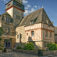 Historiske bindingsværkshuse og stentårn under blå himmel i Quiberon, Bretagne, Frankrig, med mennesker omkring.