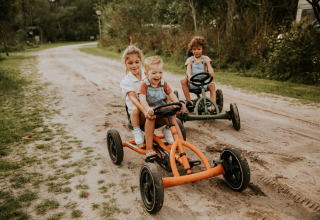 Kinderen rijden op skelters op een zandweg in het vakantiepark Camping Si-Es-An in Overijssel, Nederland.
