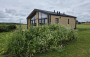 Type Dommel lodge at De Tien Heugten in the Netherlands, surrounded by green vegetation and wildflowers.