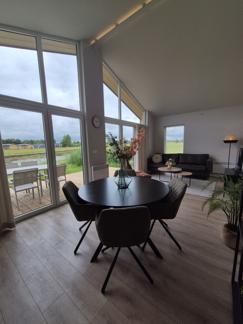 Lodge moderne avec grandes fenêtres, table ronde et canapé. Vue sur terrasse et verdure à De Tien Heugten.
