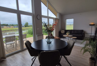 Lodge moderne avec grandes fenêtres, table ronde et canapé. Vue sur terrasse et verdure à De Tien Heugten.