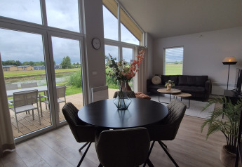 Modern lodge with large windows, round dining table, and sofa. Scenic terrace and green view at De Tien Heugten.