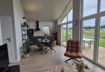 Modern lodge interior at Type Dommel, De Tien Heugten, Netherlands, with large windows, wood furniture and scenic views.