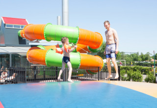 Kind en volwassene springen samen op een speelmat met glijbaan op Camping 't Veld in Overijssel, Nederland.