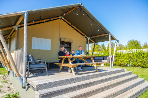 Familie nyder morgenmad udenfor deres Lodgetent 4 safari telt på en solrig dag med blå himmel.