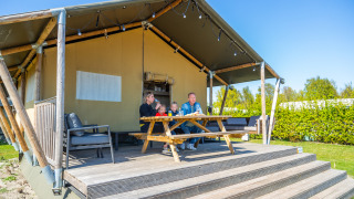 A family enjoys breakfast outdoors on the porch of their Lodgetent 4 safari tent on a sunny day.