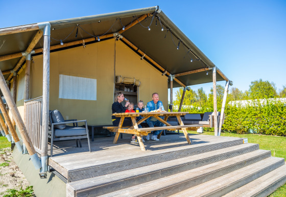 Familie nyder morgenmad udenfor deres Lodgetent 4 safari telt på en solrig dag med blå himmel.