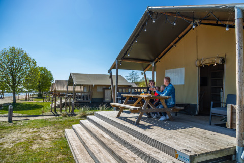 Family enjoys breakfast outside Lodgetent 4 safari tent at Zuiderzee in the Netherlands on a sunny morning.