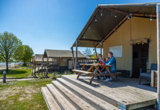 Family enjoys breakfast outside Lodgetent 4 safari tent at Zuiderzee in the Netherlands on a sunny morning.